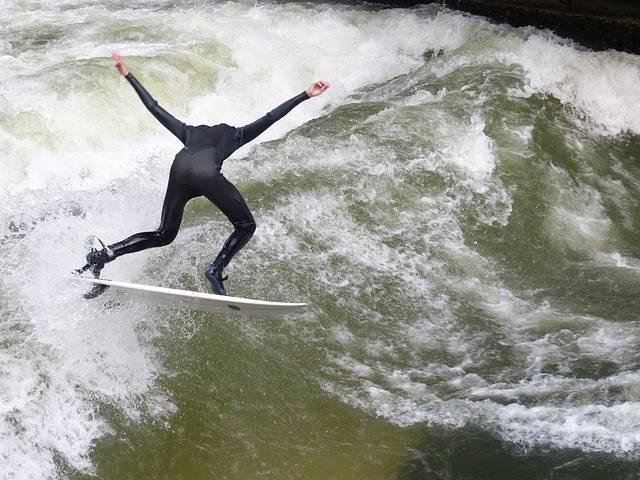 Klassenfahrt München-die Eisbachwelle wurde unter die Top 100 der schönsten Strände weltweit gewählt. Auf dem Bild sehen wir einen Surfer, der mit ausgebreiteten Armen die Welle surft.